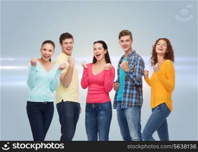 friendship, teamwork, gesture and people concept - group of smiling teenagers showing triumph gesture over gray background with laser light