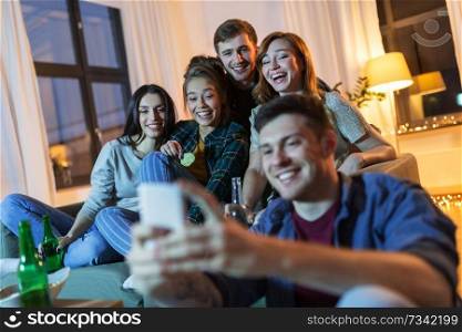 friendship, technology and entertainment concept - happy friends with smartphone, snacks and non-alcoholic drinks hanging out at home in evening. friends with smartphone and drinks at night home