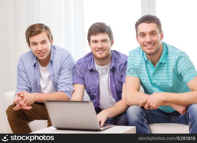 friendship, technology and home concept - smiling male friends with laptop computer at home