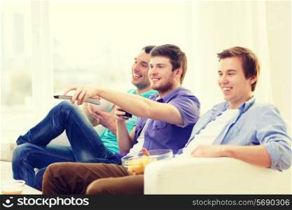 friendship, technology and home concept - smiling male friends with remote control and junk food at home