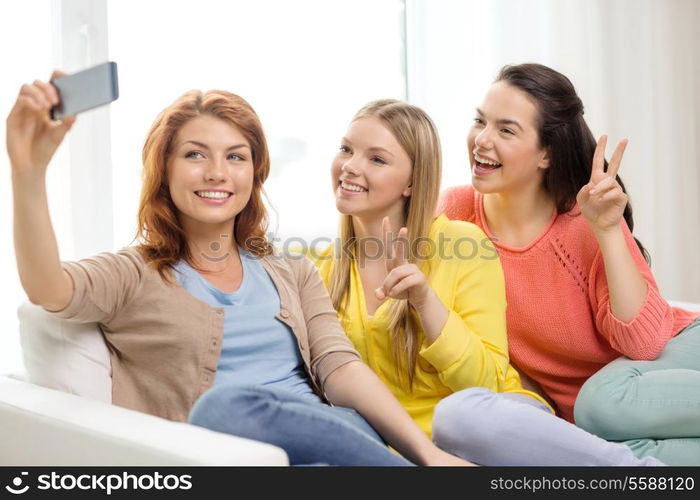 friendship, technology and internet concept - three smiling teenage girls taking picture with smartphone camera at home