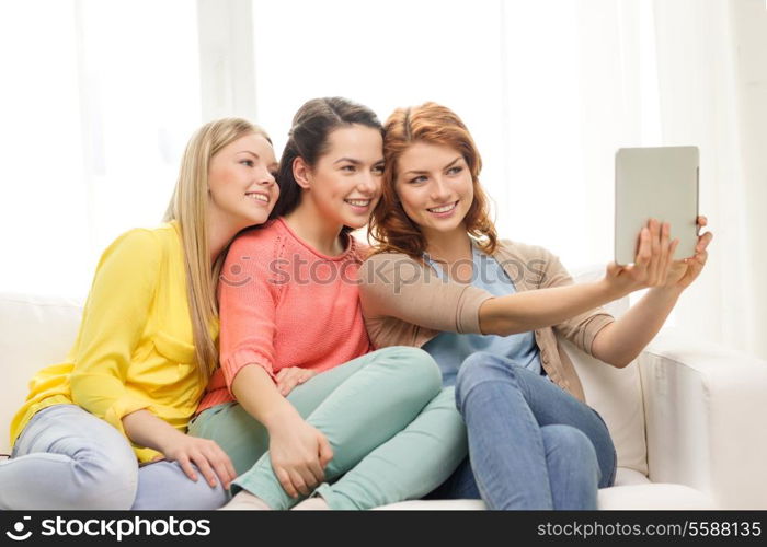 friendship, technology and internet concept - three smiling teenage girls taking picture with tablet pc computer camera at home