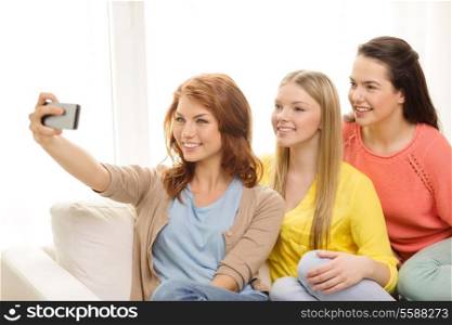 friendship, technology and internet concept - three smiling teenage girls taking picture with smartphone camera at home