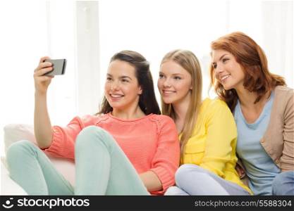 friendship, technology and internet concept - three smiling teenage girls taking picture with smartphone camera at home