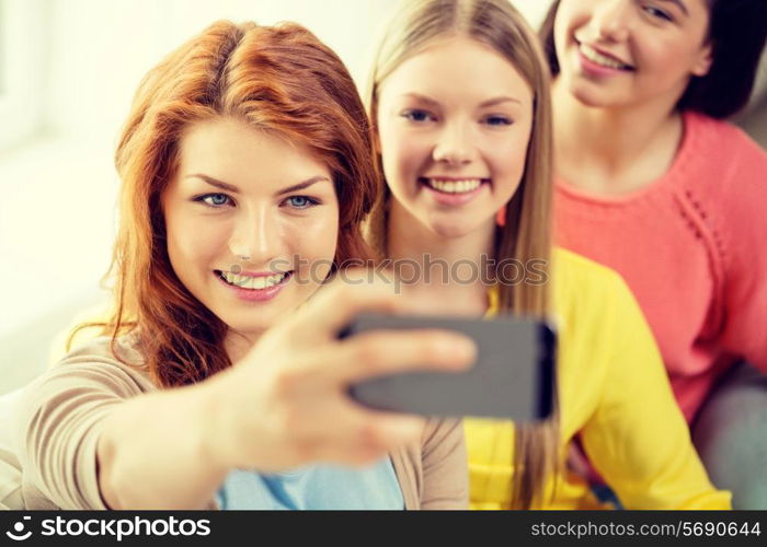 friendship, technology and internet concept - three smiling teenage girls taking picture with smartphone camera at home