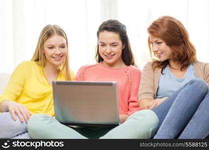 friendship, technology and internet concept - three smiling teenage girls with laptop computer at home