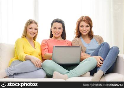 friendship, technology and internet concept - three smiling teenage girls with laptop computer at home
