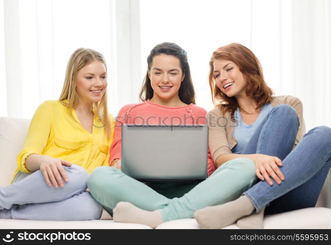 friendship, technology and internet concept - three smiling teenage girls with laptop computer at home