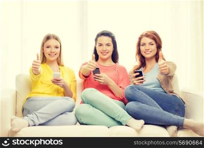 friendship, technology and internet concept - three smiling teenage girls with smartphones at home showing thumbs up