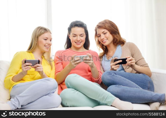 friendship, technology and internet concept - three smiling teenage girls with smartphones at home