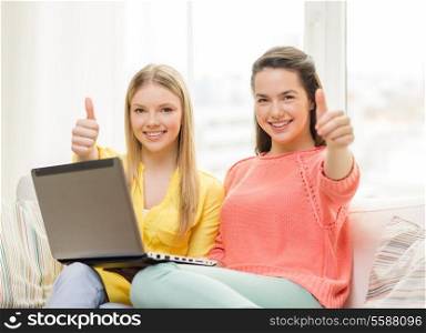 friendship, technology and internet concept - two smiling teenage girls with laptop computer at home showing thumbs up