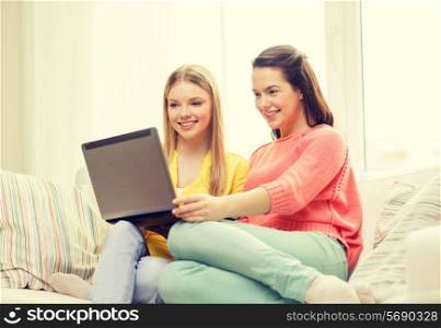 friendship, technology and internet concept - two smiling teenage girls with laptop computer at home