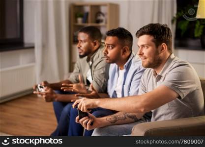 friendship, technology and leisure concept - male friends with gamepads and beer playing video game at home at night. happy friends playing video games at home at night