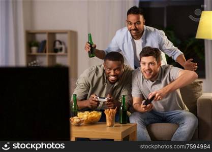 friendship, technology and leisure concept - smiling male friends with gamepads and beer playing video game at home at night. happy friends playing video games at home at night