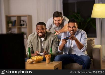 friendship, technology and leisure concept - smiling male friends with gamepads and beer playing video game at home at night. happy friends playing video games at home at night