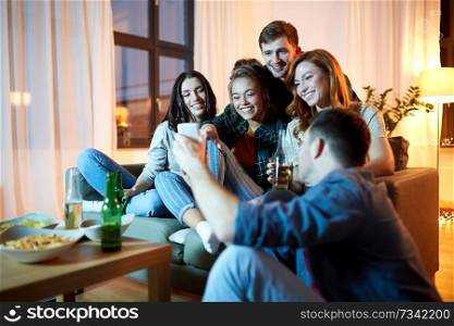 friendship, technology and party concept - happy friends with smartphone, snacks and non-alcoholic drinks at home in evening. happy friends with smartphone at home party