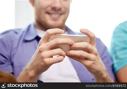 friendship, technology and people concept - close up of happy man with smartphone texting or playing games at home