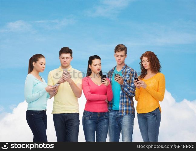 friendship, technology and people concept - group of serious teenagers with smartphones over blue sky with white cloud background
