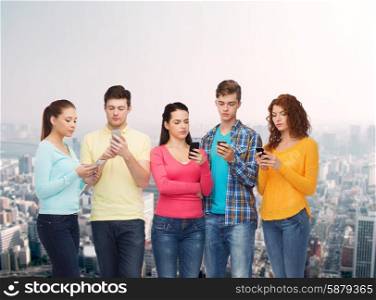 friendship, technology and people concept - group of serious teenagers with smartphones over city background
