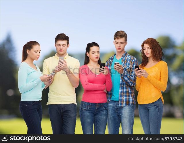 friendship, technology and people concept - group of serious teenagers with smartphones over park background