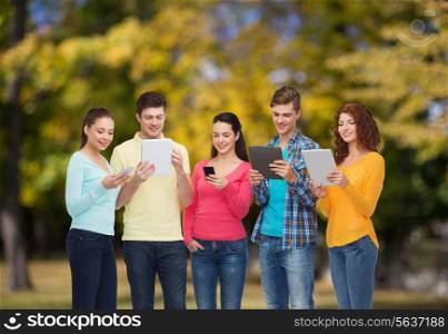 friendship, technology and people concept - group of smiling teenagers with smartphones and tablet pc computers over park background