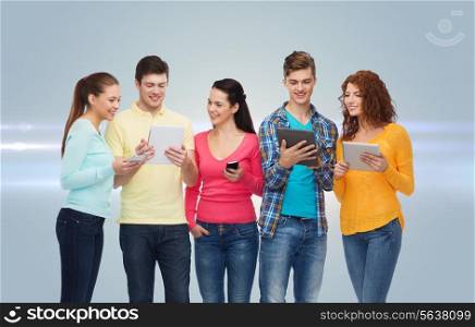friendship, technology and people concept - group of smiling teenagers with smartphones and tablet pc computers over gray background with laser light