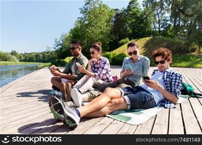 friendship, technology and travel concept - group of friends with smartphone on lake pier in summer. friends with smartphone on lake pier in summer