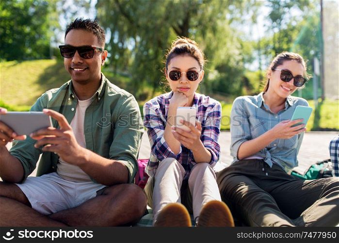 friendship, technology and travel concept - group of friends with smartphones at summer park. friends with smartphones at summer park