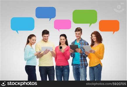 friendship, technology, communication and people concept - group of smiling teenagers with smartphones and tablet pc computers over messenger text bubbles and gray background