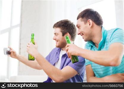 friendship, technology, drinks and home concept - smiling male friends with smartphone and beer at home