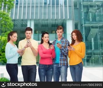 friendship, technology, education, business and people concept - group of serious teenagers with smartphones over campus background