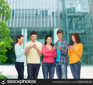 friendship, technology, education, business and people concept - group of smiling teenagers with smartphones over campus background