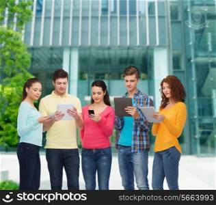 friendship, technology, education, business and people concept - group of smiling teenagers with smartphones and tablet pc computers over campus background