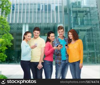 friendship, technology, education, business and people concept - group of smiling teenagers with smartphones over campus background
