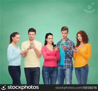 friendship, technology, education, school and people concept - group of serious teenagers with smartphones over green board background