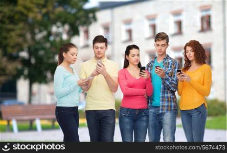 friendship, technology, education, school and people concept - group of serious teenagers with smartphones over campus background