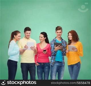 friendship, technology, education, school and people concept - group of smiling teenagers with smartphones and tablet pc computers over green board background