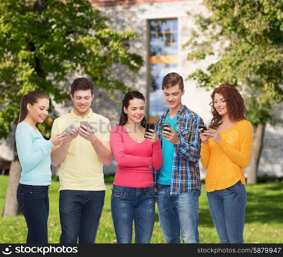 friendship, technology, education, school and people concept - group of smiling teenagers with smartphones over campus background