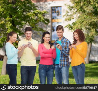 friendship, technology, education, school and people concept - group of smiling teenagers with smartphones over campus background