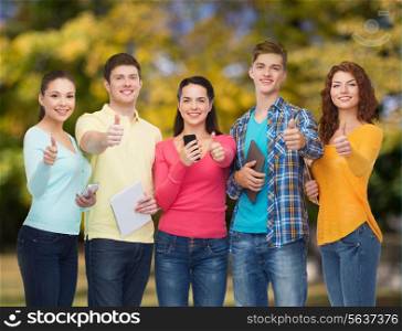 friendship, technology, gesture and people concept - group of smiling teenagers with smartphones and tablet pc computers showing thumbs up over park background