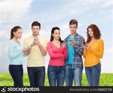 friendship, technology, nature and people concept - group of serious teenagers with smartphones over blue sky and grass background