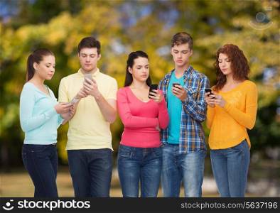 friendship, technology, nature and people concept - group of serious teenagers with smartphones over park background