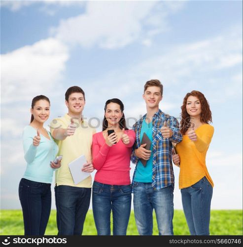 friendship, technology, summer and people concept - group of smiling teenagers with smartphones and tablet pc computers showing thumbs up