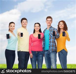friendship, technology, summer and people concept - group of smiling teenagers with smartphones over blue sky and grass background