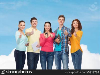 friendship, technolpgy and people concept - group of smiling teenagers with smartphones and tablet pc computers showing thumbs up over blue sky with white cloud background