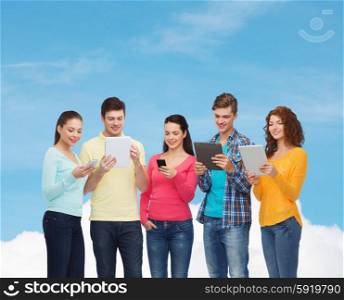 friendship, technolpgy and people concept - group of smiling teenagers with smartphones and tablet pc computers over blue sky with white cloud background