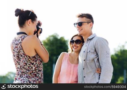 friendship, tourism, summer, technology and people concept - happy friends with camera taking picture outdoors