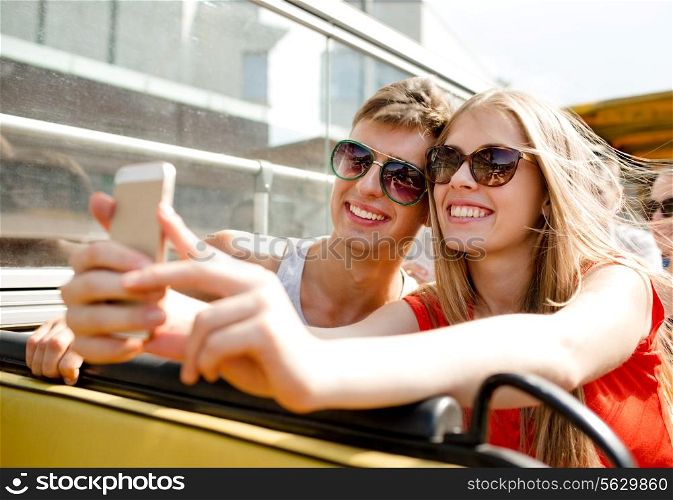 friendship, tourism, summer vacation, technology and people concept - smiling couple with smartphone traveling by tour bus and making selfie