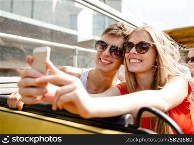 friendship, tourism, summer vacation, technology and people concept - smiling couple with smartphone traveling by tour bus and making selfie
