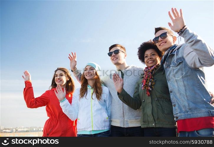 friendship, tourism, travel and people concept - group of happy teenage friends in sunglasses hugging and waving hands outdoors